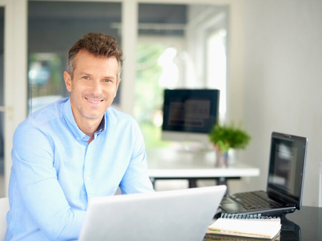 Happy businessman wearing shirt while sitting at office desk and using his computer.